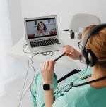 Frau mit Kopfhörern auf den Ohren in grüner Klinkarbeitskleidung vor einem Laptop