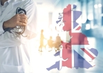 Teaserbild das für den Nationalen Gesundheitsdienst in UK stehen soll. Es ist der Oberkörper eines Arztes abgebildet, im Hintergrund ein Krankenhausflur. Rechts vom Arzt ist der leicht transparente Umriss der britischen Flagge abgebildet in Form von Großbritannien.